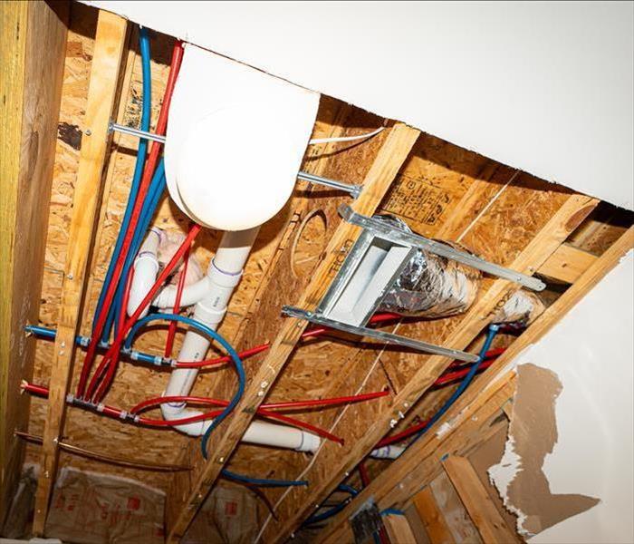 Ceiling with exposed wooden beams, insulation, and pipes, showcasing plumbing and electrical work in progress, featuring PEX 